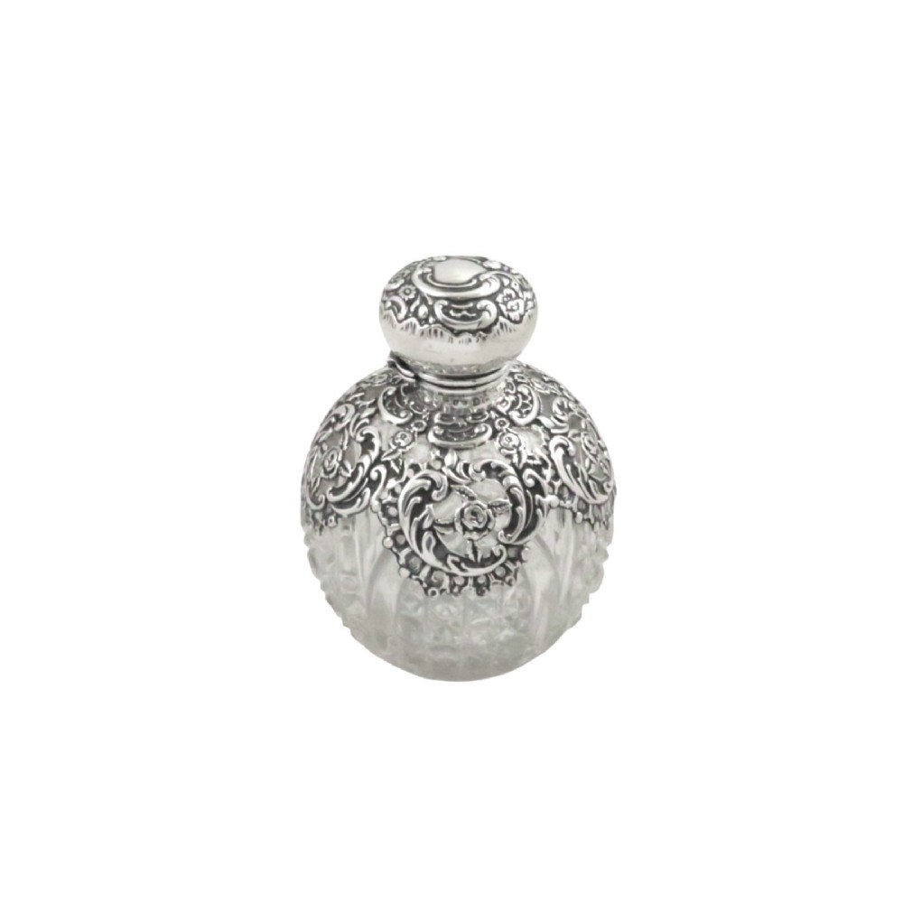 An Edwardian clear glass scent bottle featuring a round body with ornate embossed sterling silver overlay and matching cap.