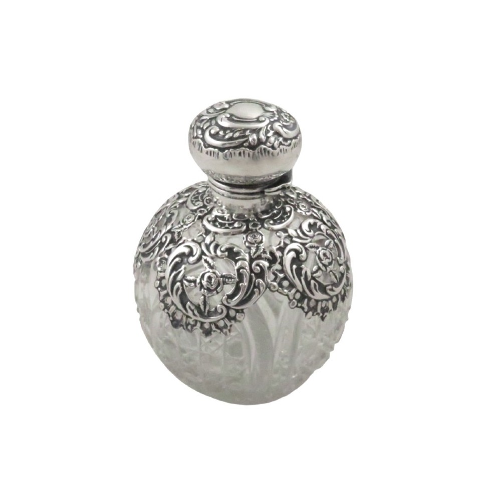 An Edwardian clear glass scent bottle featuring a round body with ornate embossed sterling silver overlay and matching cap. View VII