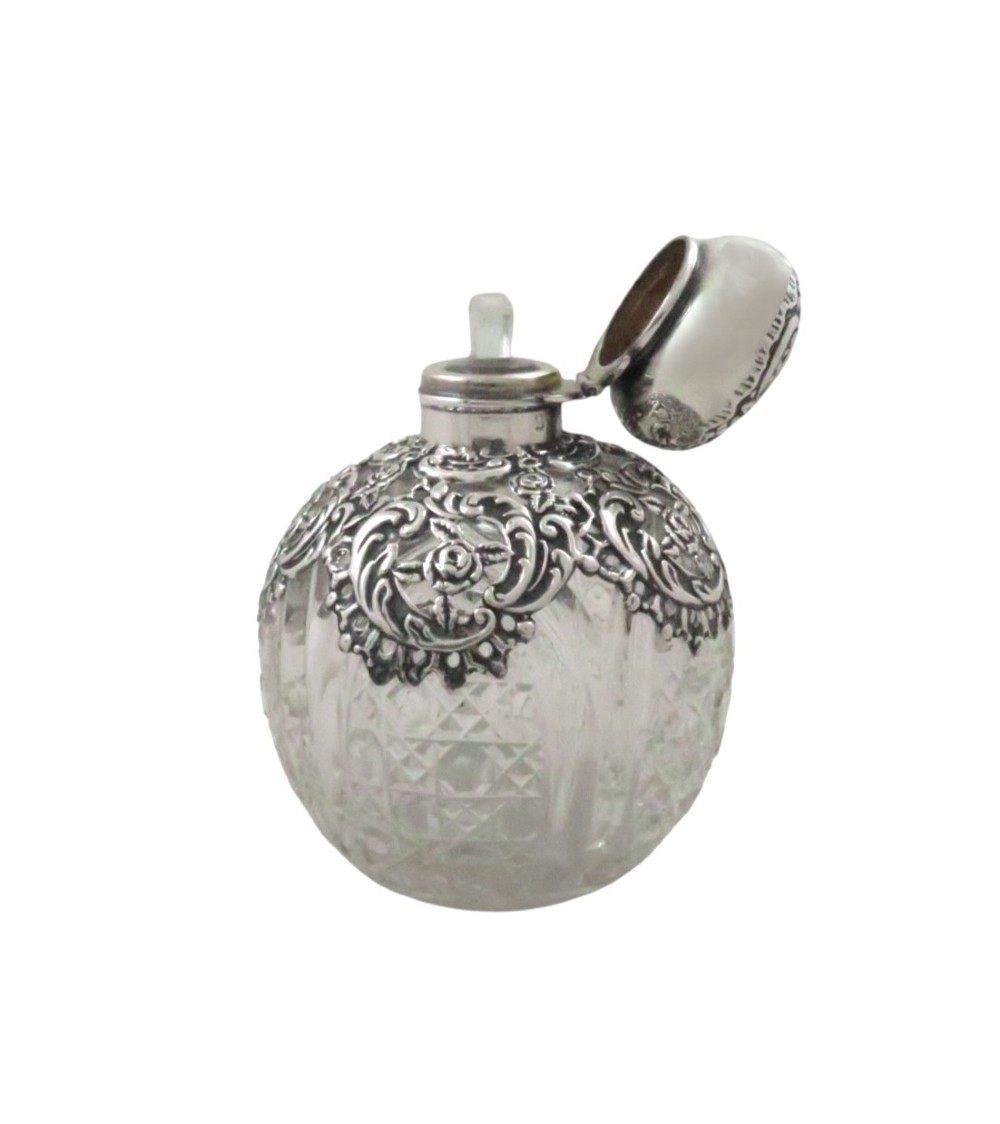 An Edwardian clear glass scent bottle featuring a round body with ornate embossed sterling silver overlay and matching cap. View VIII