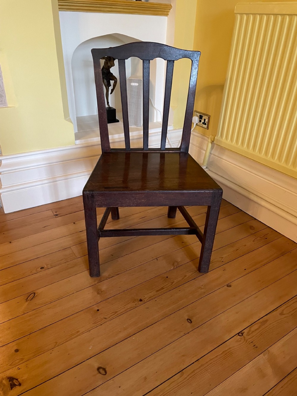 A late Georgian dark mahogany country chair featuring a four-slat backrest, shaped top rail, solid wood seat, and square legs reinforced with H-stretchers.