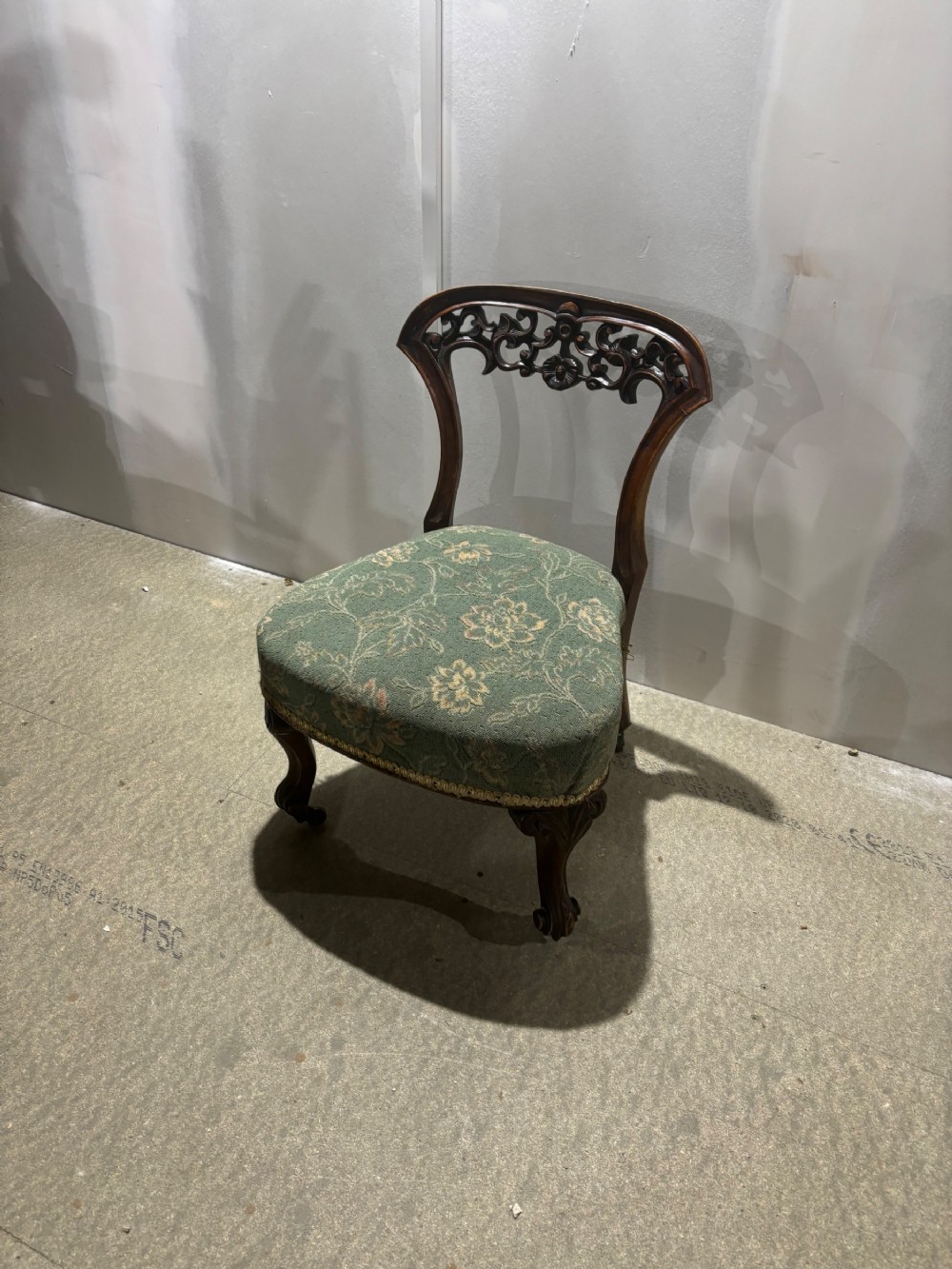 A Victorian walnut nursing chair featuring a low upholstered green floral seat, carved openwork backrest, and cabriole front legs.