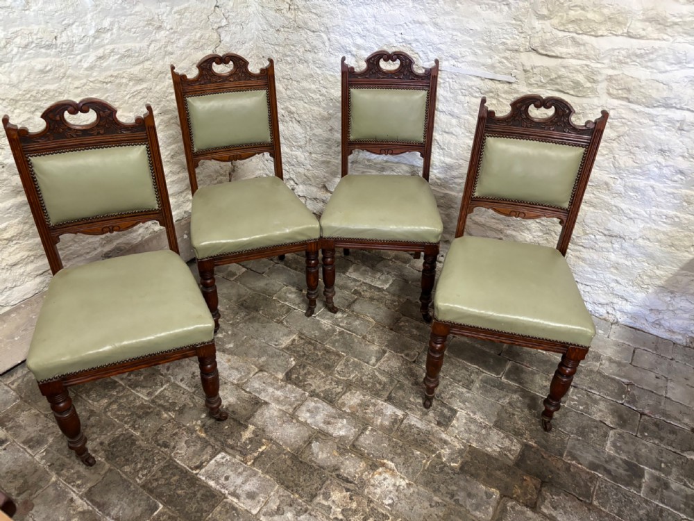 A set of four late Victorian carved oak dining chairs featuring sage green leather padded seats and backrests with brass stud detailing.