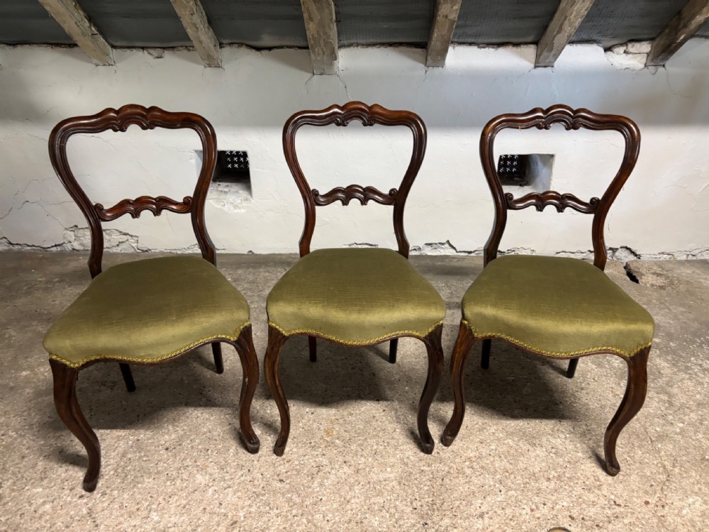 A set of three 19th-century Victorian rosewood balloon back dining chairs featuring carved crest rails, olive green upholstered seats, and cabriole front legs.