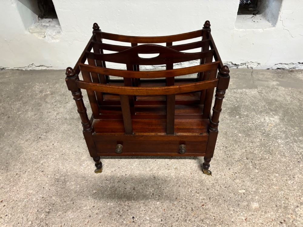 A Victorian mahogany Canterbury featuring slatted top compartments, turned corner posts with finials, a lower drawer, and brass castors.