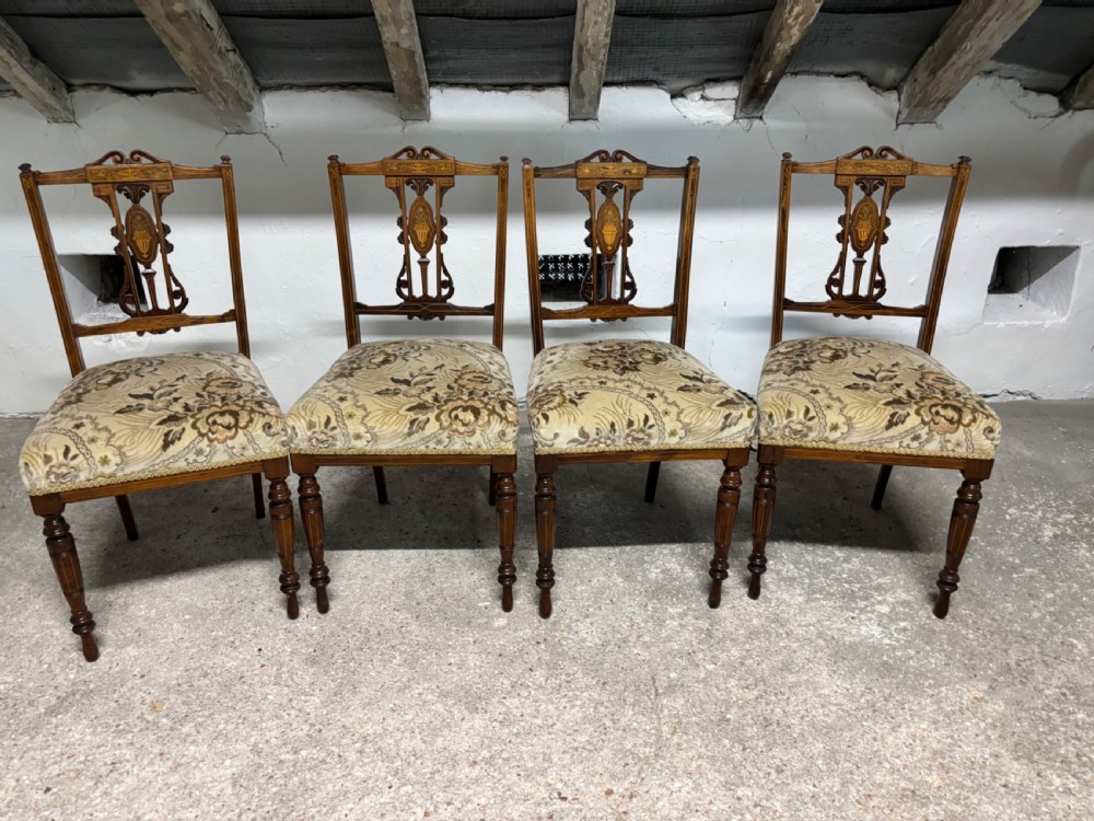 A set of four Edwardian rosewood salon chairs featuring floral pattern upholstery, turned front legs, and central urn marquetry inlays on the backrests.