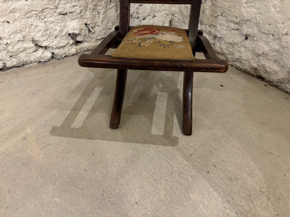 A dark oak Victorian childs folding chair with barley twist side supports, carved cresting top, and floral needlepoint fabric on the backrest and seat. View IV