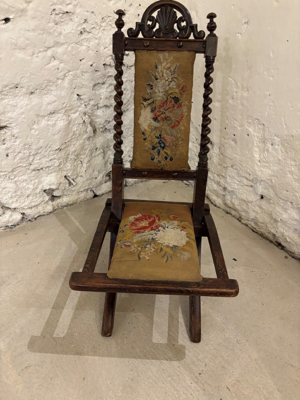 A dark oak Victorian childs folding chair with barley twist side supports, carved cresting top, and floral needlepoint fabric on the backrest and seat.