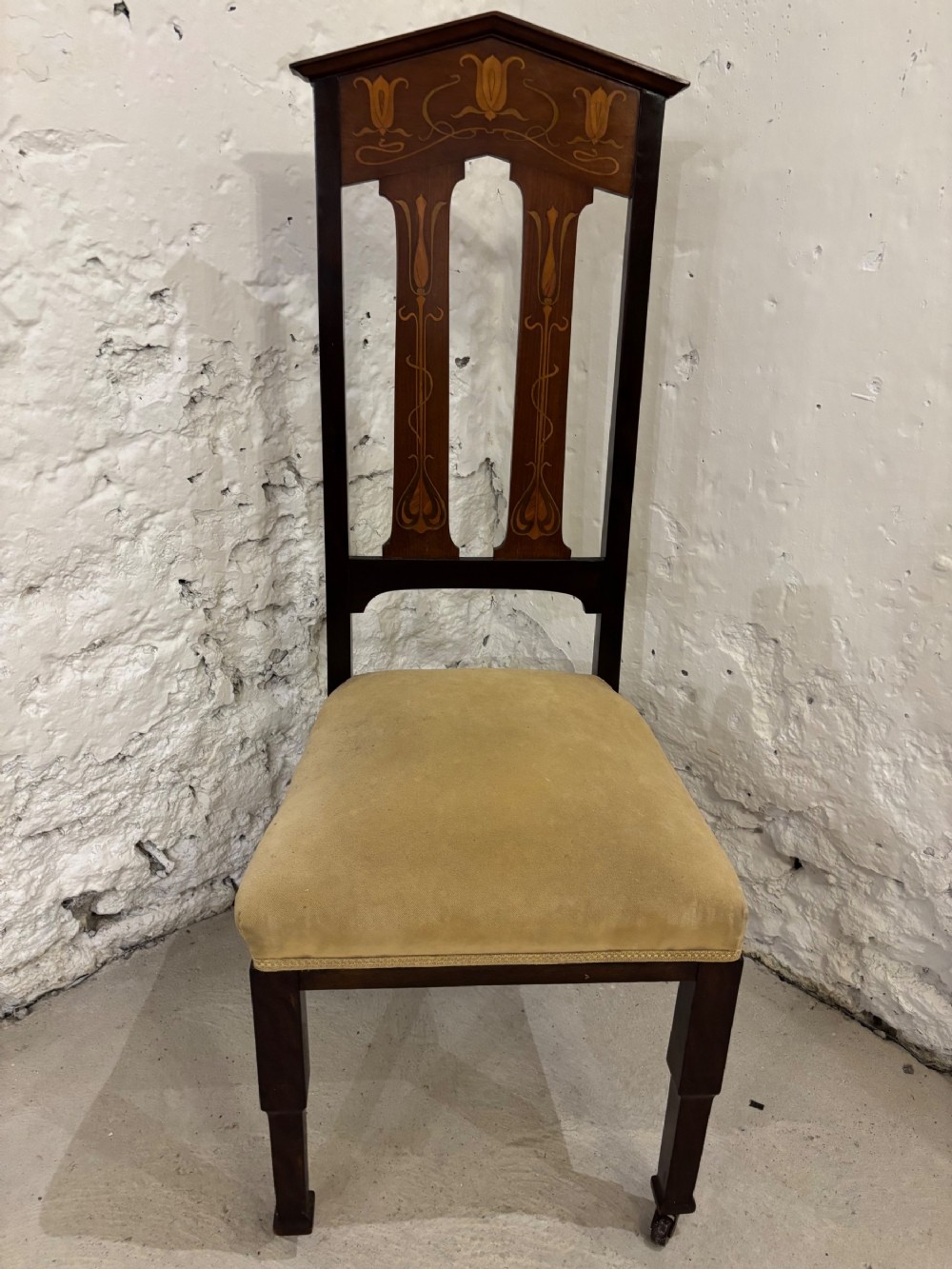 An Edwardian dark mahogany high-backed side chair featuring Art Nouveau floral marquetry inlay on the backrest and a light yellow upholstered seat.