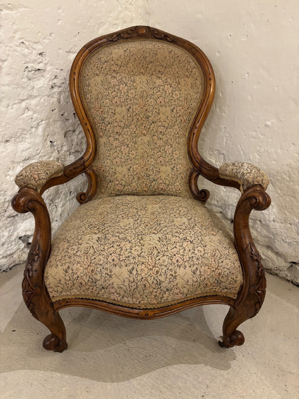 A Victorian open-armed gentlemans armchair with a carved walnut frame, beige floral tapestry upholstery, and cabriole legs.