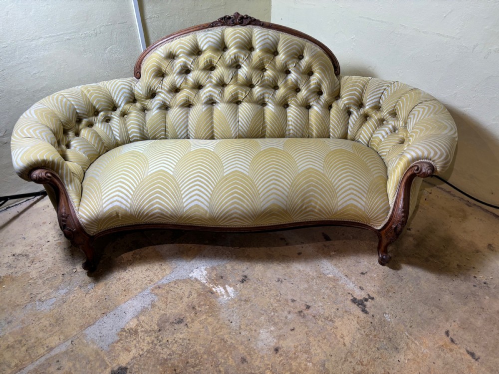 A Victorian carved walnut sofa featuring a curved, deep-buttoned back upholstered in a yellow patterned fabric resting on short cabriole legs.