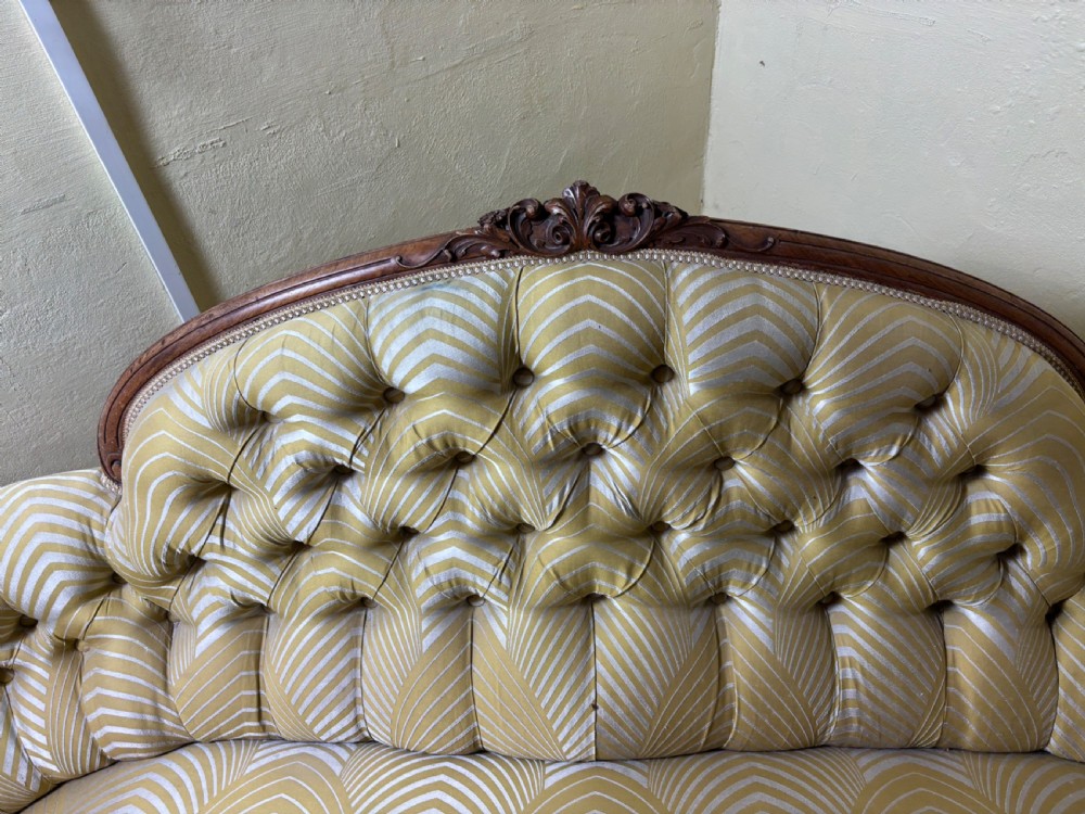 A Victorian carved walnut sofa featuring a curved, deep-buttoned back upholstered in a yellow patterned fabric resting on short cabriole legs. View II