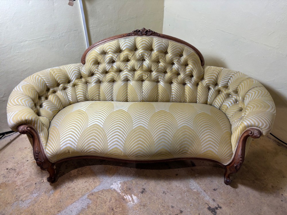 A Victorian carved walnut sofa featuring a curved, deep-buttoned back upholstered in a yellow patterned fabric resting on short cabriole legs. View V