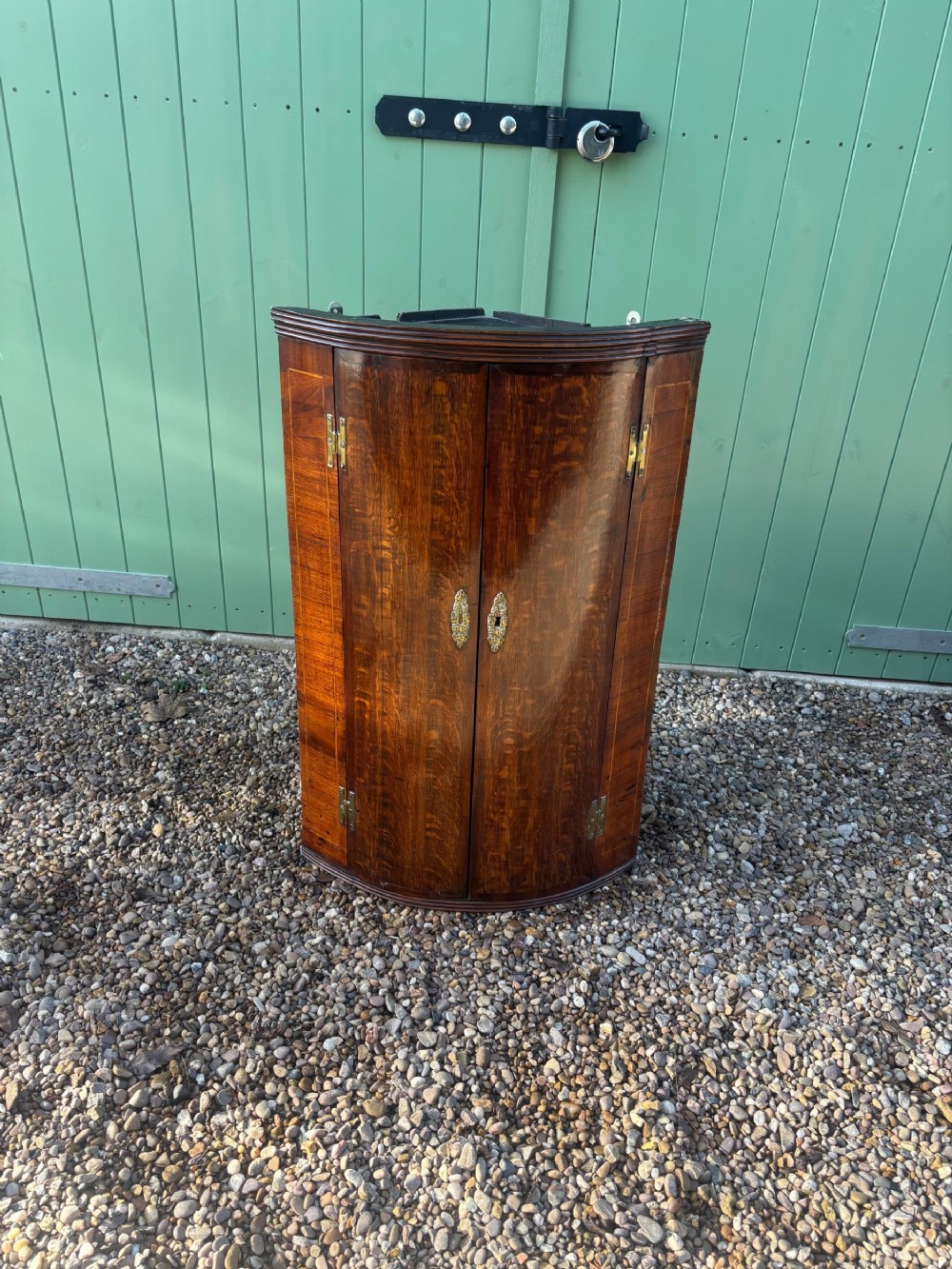 A Georgian bowfront oak and mahogany hanging corner cupboard featuring double doors with brass escutcheons and external brass hinges.