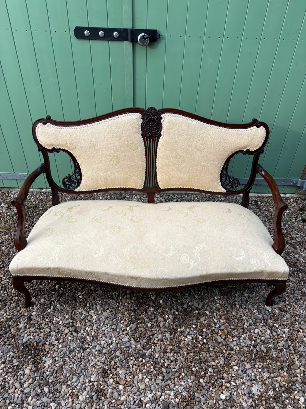 An Edwardian carved mahogany parlour sofa featuring a double-contoured backrest upholstered in cream damask fabric and supported by cabriole legs.