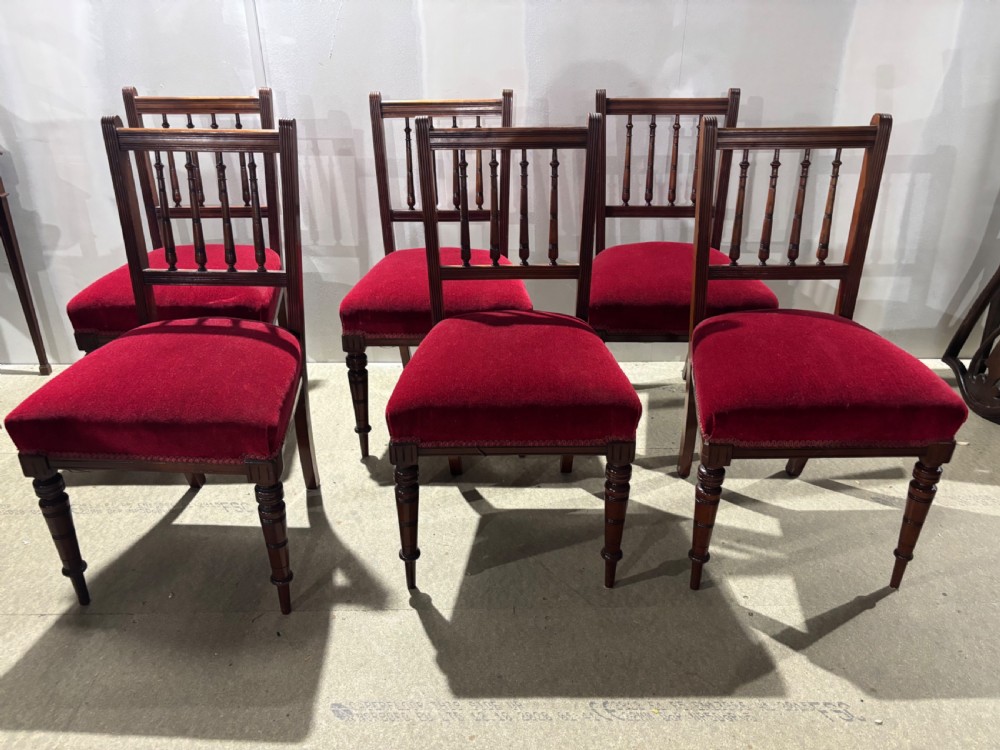 A set of six late Victorian dark walnut dining chairs featuring spindle backrests and red velvet upholstered seats.