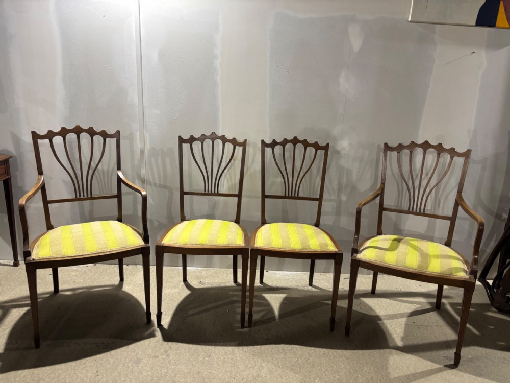 A set of four Edwardian mahogany salon chairs featuring fan-shaped pierced back splats, subtle string inlay, slender tapered legs, and yellow striped fabric seat cushions.
