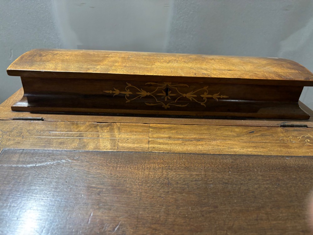 A Victorian walnut Davenport desk featuring floral boxwood marquetry inlay, an inset leather writing slope, and turned feet with castors. View II