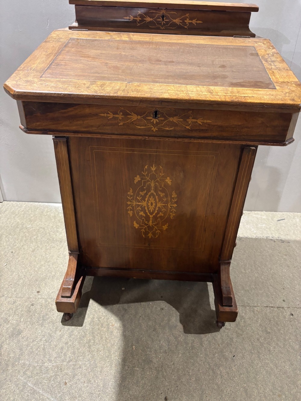 A Victorian walnut Davenport desk featuring floral boxwood marquetry inlay, an inset leather writing slope, and turned feet with castors.