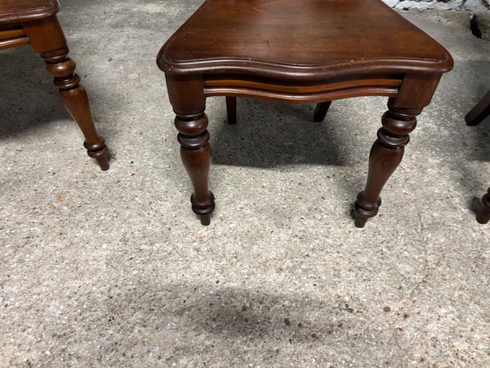 A set of three Victorian mahogany hall chairs with carved scrollwork backs, central shield motifs, solid timber seats, and turned front legs. View II