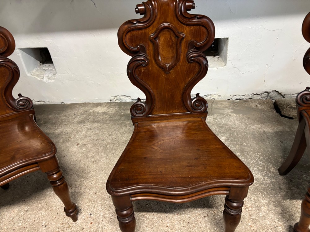A set of three Victorian mahogany hall chairs with carved scrollwork backs, central shield motifs, solid timber seats, and turned front legs. View III