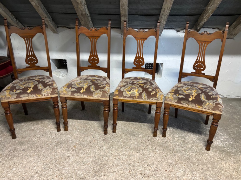A set of four Edwardian walnut dining chairs featuring carved back splats, turned front legs, and floral patterned fabric seats.