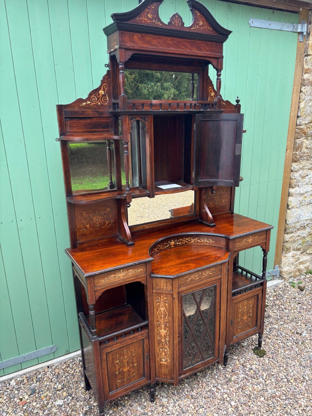 A late Victorian rosewood side cabinet featuring floral marquetry inlays, bevelled glass mirror panels, tiered shelving, and a central glazed door cupboard.