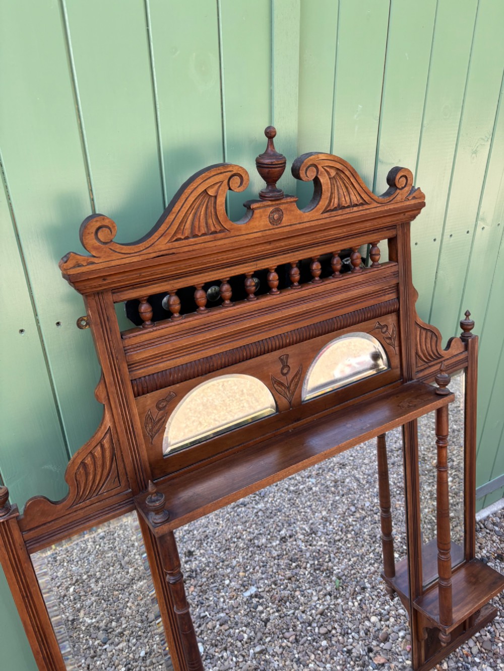 An Edwardian carved walnut overmantel mirror featuring multiple glass plates, integrated display shelves, turned columns, and a decorative crest with a central finial. View II
