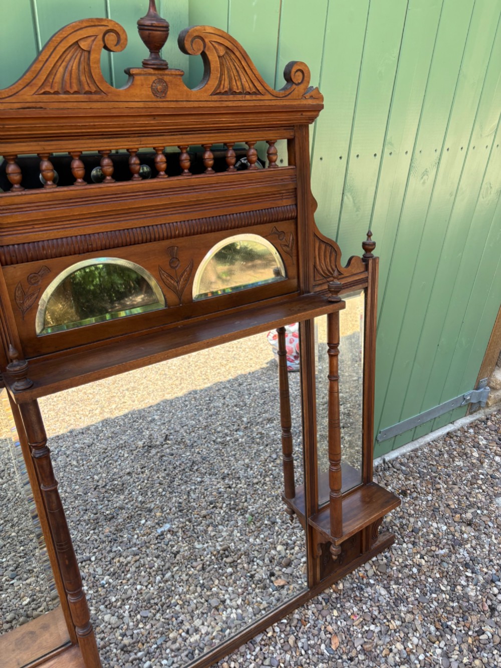 An Edwardian carved walnut overmantel mirror featuring multiple glass plates, integrated display shelves, turned columns, and a decorative crest with a central finial. View IV