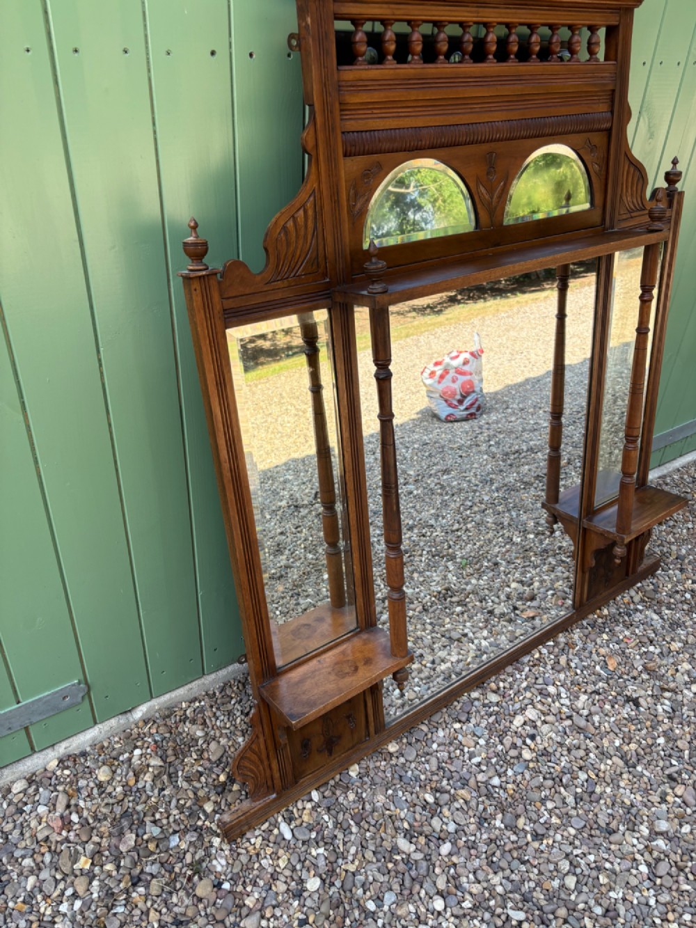 An Edwardian carved walnut overmantel mirror featuring multiple glass plates, integrated display shelves, turned columns, and a decorative crest with a central finial. View V
