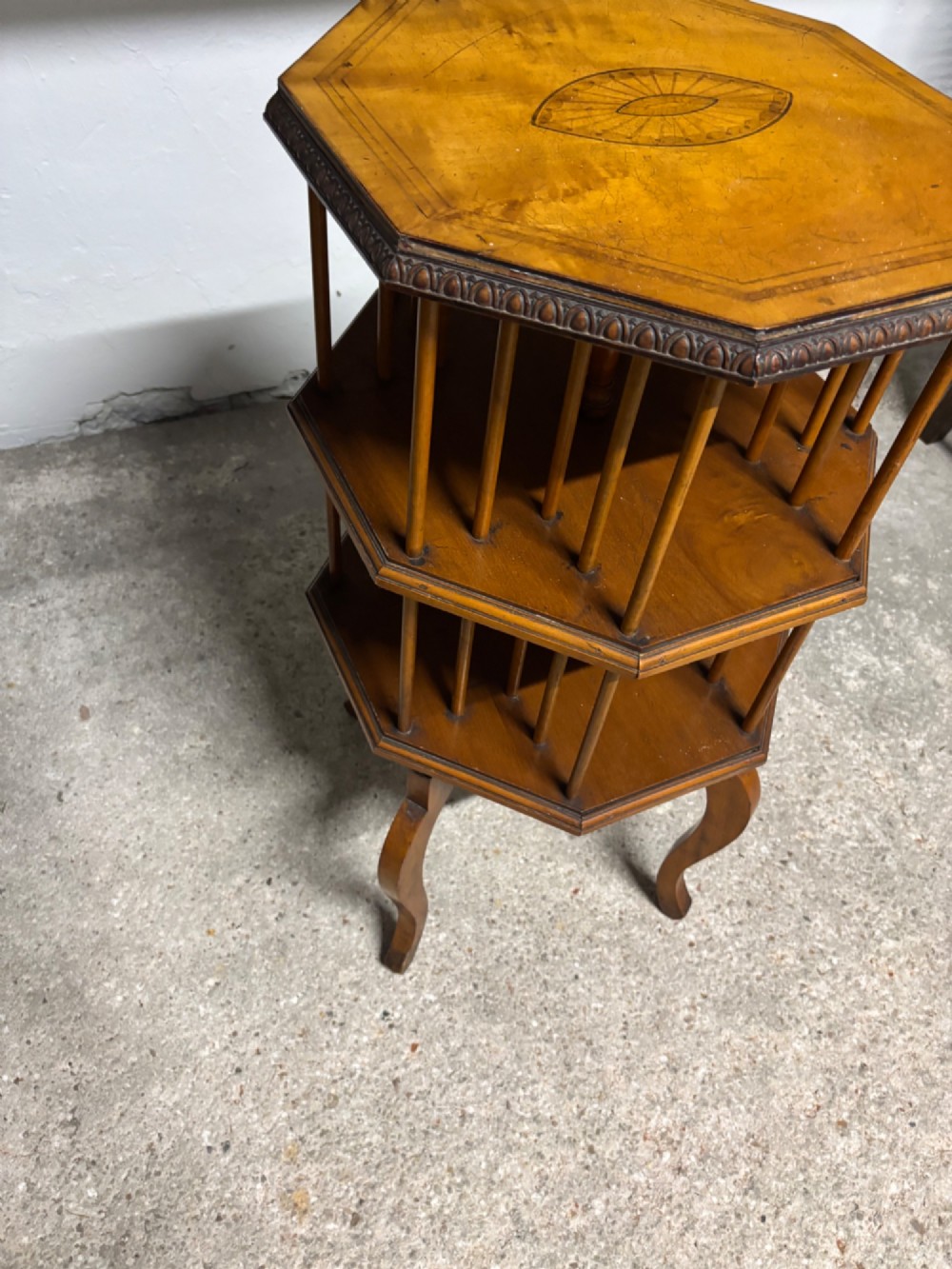 An Edwardian octagonal satinwood revolving bookcase featuring central marquetry inlay, spindle supports, two open tiers, and cabriole legs. View V