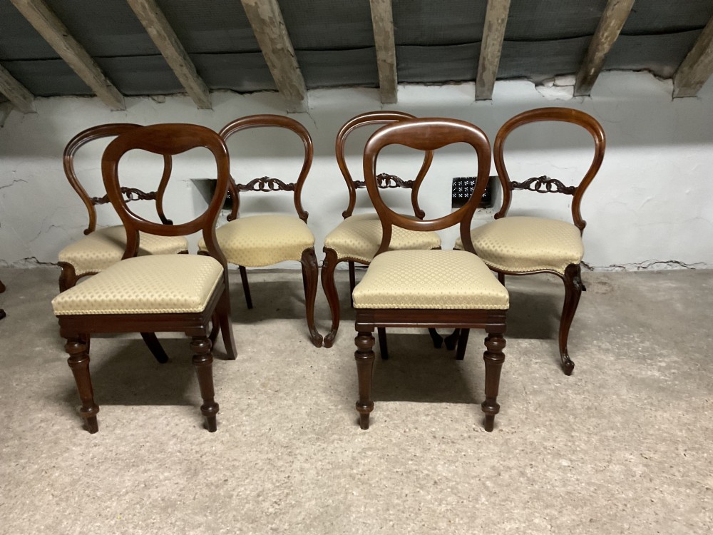 A set of six Victorian balloon back dining chairs in dark wood with cream patterned upholstered seats.