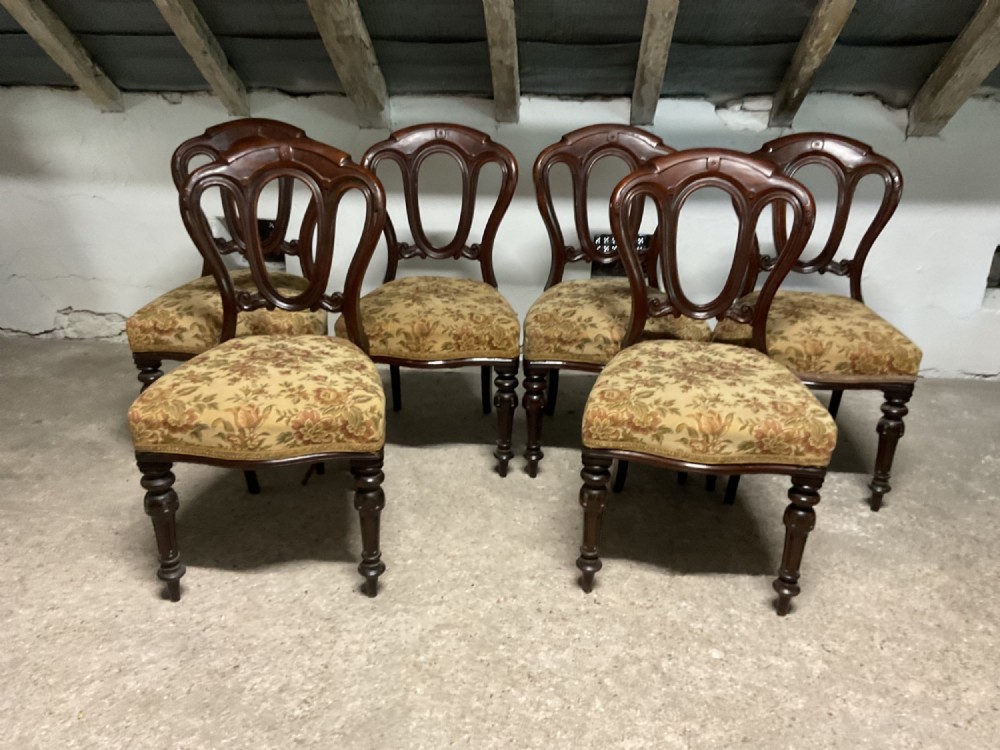 A set of six Victorian mahogany dining chairs featuring balloon backs, carved backrests, turned front legs, and floral patterned upholstered seats.