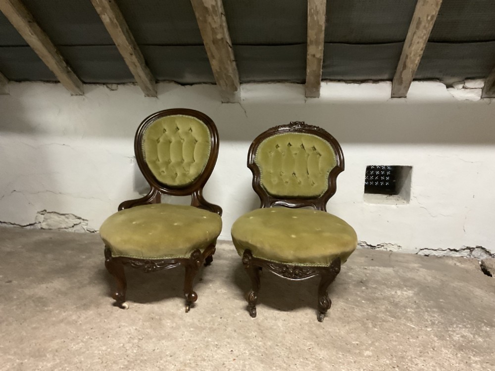 A pair of Victorian mahogany low-seated nursing chairs upholstered in olive green button-backed velvet with carved cabriole legs on castors.