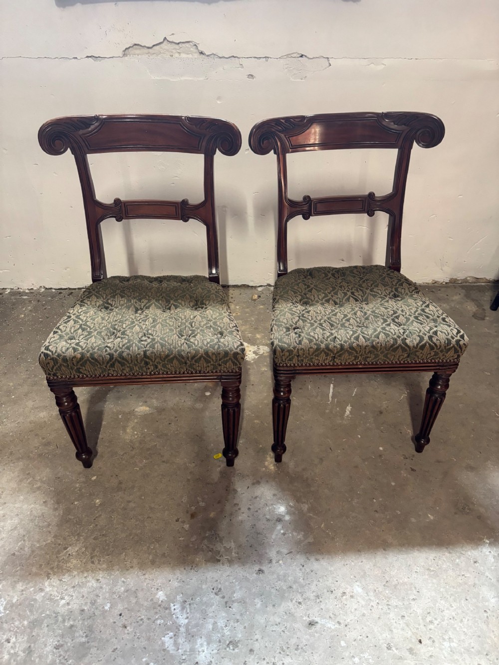 A pair of antique William IV mahogany side chairs featuring scroll top rails, fluted turned legs, and green patterned fabric seats.