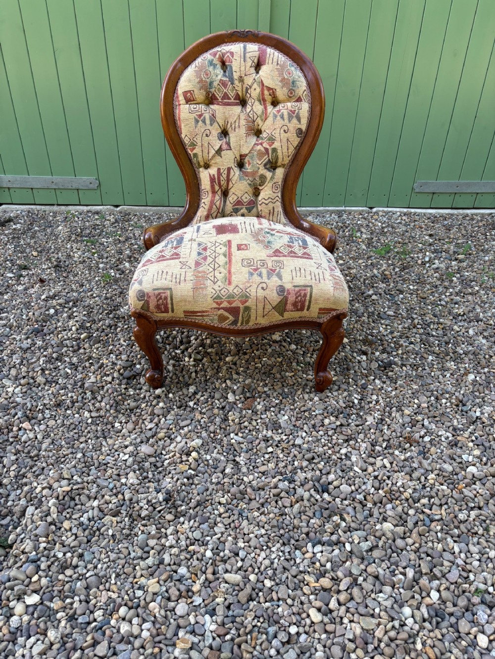 A low Victorian mahogany nursing chair featuring deep button-backed upholstery and carved cabriole legs.