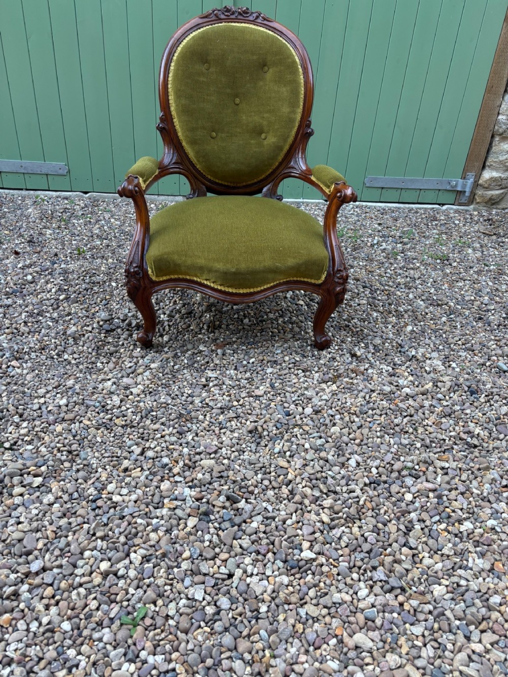 A Victorian carved mahogany open armchair upholstered in olive green velvet with a buttoned oval backrest and cabriole legs.