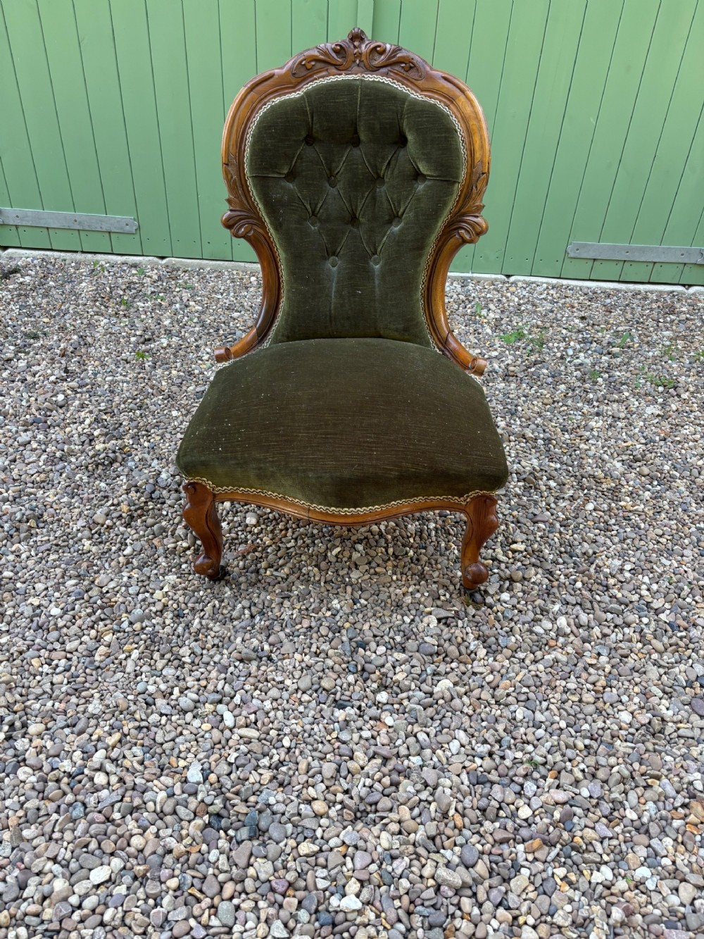 A low-seated Victorian mahogany nursing chair upholstered in deep buttoned olive green velvet with carved frame details and cabriole legs on brass castors.
