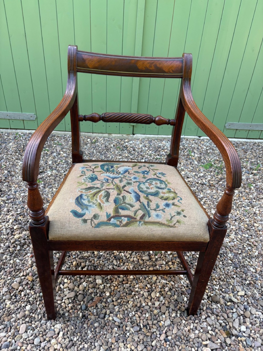 A Regency period mahogany open armchair featuring sweeping curved armrests, a turned rope-twist back bar, and a floral needlepoint seat.