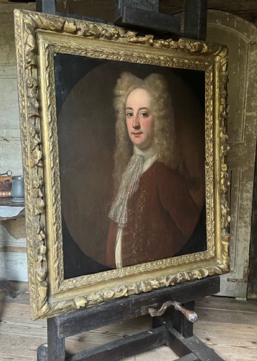 fig 1. An early 18th-century oil portrait depicting a gentleman in a crimson coat and powdered wig, set within a heavily carved gilded frame.