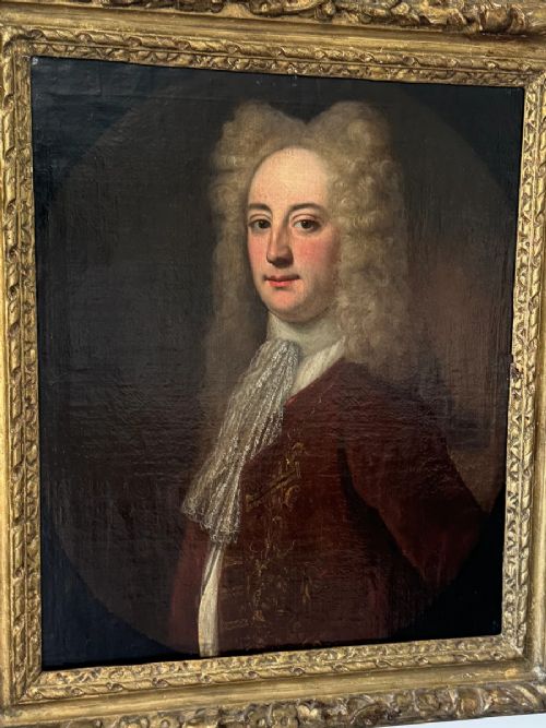 An early 18th-century oil portrait depicting a gentleman in a crimson coat and powdered wig, set within a heavily carved gilded frame. View XI