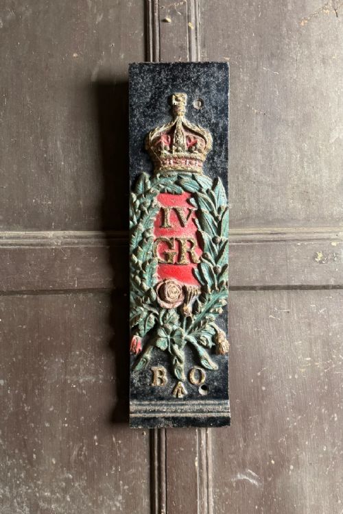 fig 1. A vertical rectangular cast iron plaque featuring a painted crown, laurel wreath surrounding the letters IV GR, and the initials B O at the base.