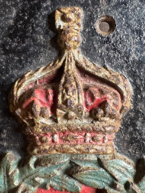 fig 3. A vertical rectangular cast iron plaque featuring a painted crown, laurel wreath surrounding the letters IV GR, and the initials B O at the base.