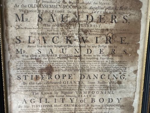 fig 2. An 18th-century paper handbill with black letterpress typography advertising performance acts, displayed in a black frame with a gilt inner border.