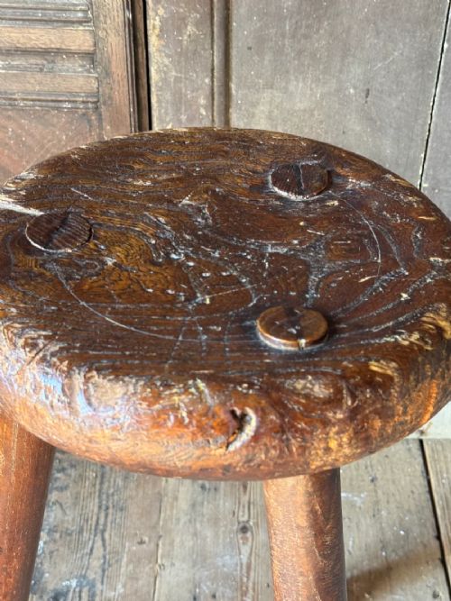 A 19th-century rustic three-legged wooden stool featuring a thick dished circular elm seat and splayed turned legs. View V