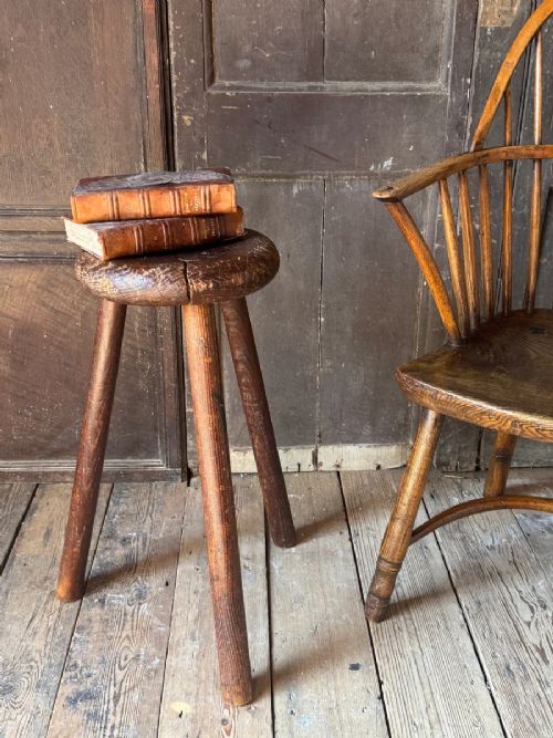 A 19th-century rustic three-legged wooden stool featuring a thick dished circular elm seat and splayed turned legs. View VII