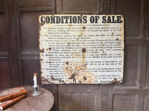 fig 1. A rectangular off-white painted sheet metal sign featuring bold black typography detailing auction conditions of sale, with visible surface rust and paint wear.