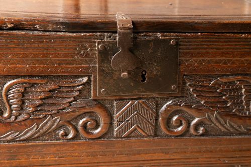 fig 2. An Elizabethan carved oak boarded chest featuring relief carvings of winged mythical beasts, an iron lockplate, and slab end legs.