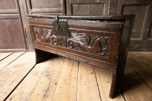 fig 7. An Elizabethan carved oak boarded chest featuring relief carvings of winged mythical beasts, an iron lockplate, and slab end legs.