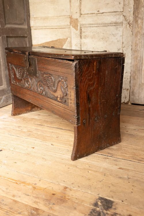 fig 8. An Elizabethan carved oak boarded chest featuring relief carvings of winged mythical beasts, an iron lockplate, and slab end legs.