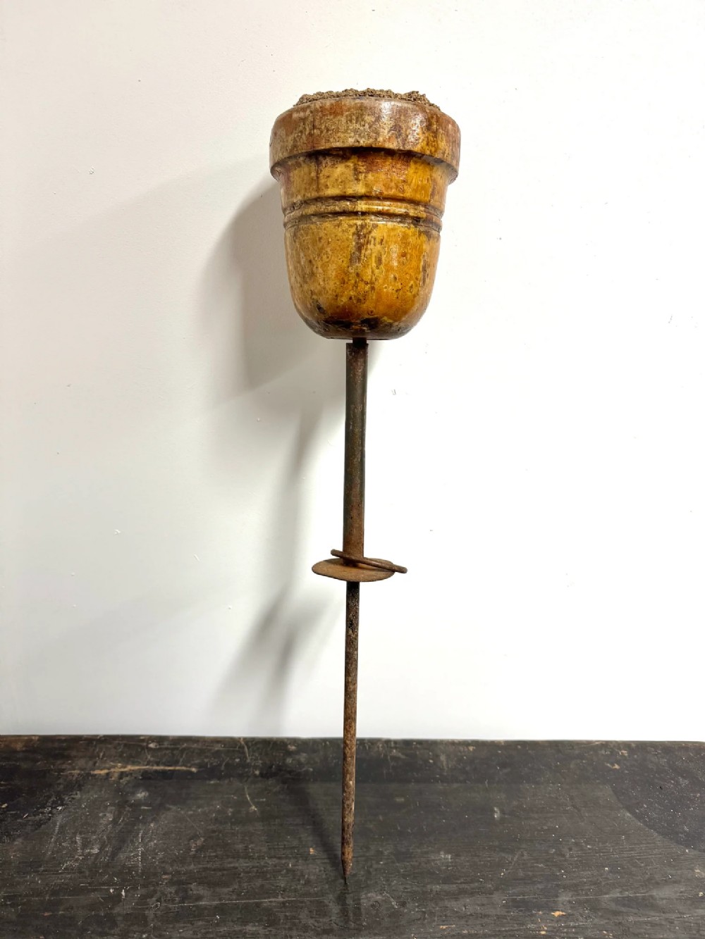 A turned wooden falconry block mounted on a long iron ground spike with a circular metal flange.